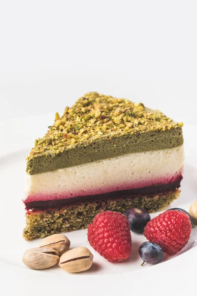 Close up view of sweet cake with pistachios and berries on plate isolated on white — Stock Photo