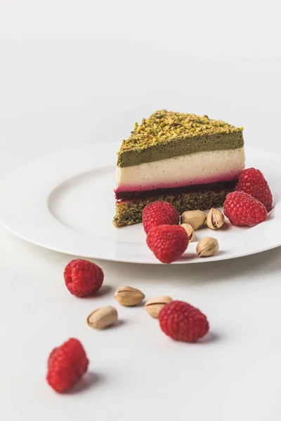 Close up view of sweet cake with pistachios and raspberries on plate isolated on white — Stock Photo