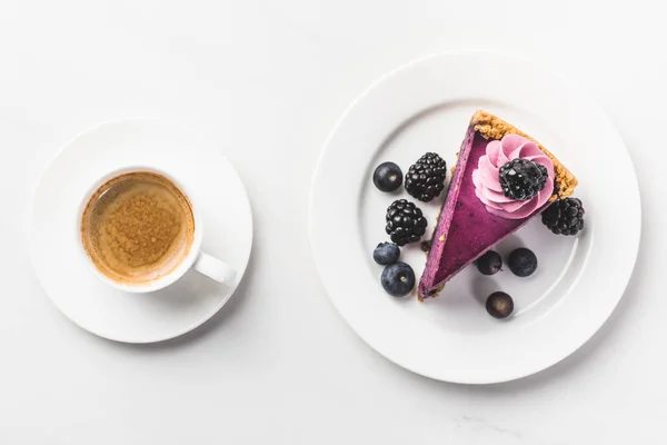 Vista superior del pedazo de pastel con bayas y taza de café aislado en la mesa blanca - foto de stock