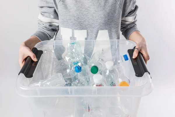 Vista parcial de la mujer sosteniendo contenedor con botellas de plástico aisladas en gris, reciclar concepto - foto de stock