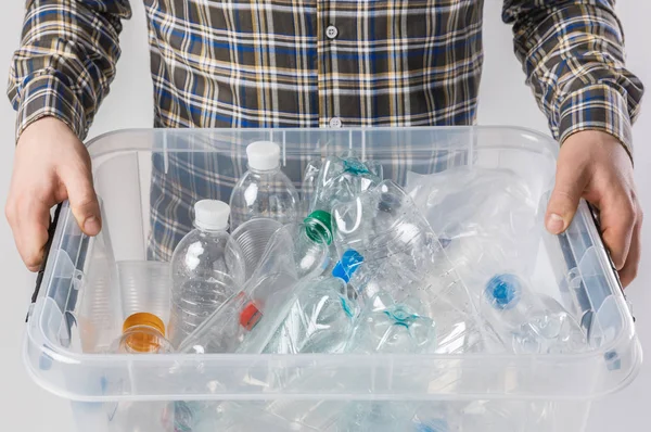 Vista parcial del hombre sosteniendo contenedor con botellas de plástico en manos aisladas en gris, concepto de reciclaje - foto de stock