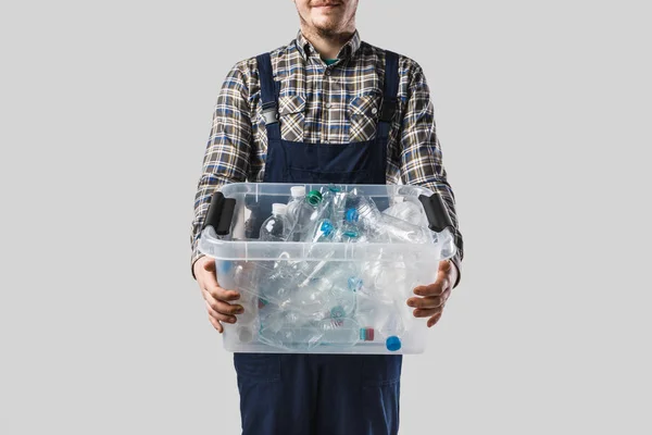 Vista parcial del hombre sosteniendo contenedor con botellas de plástico en manos aisladas en gris, concepto de reciclaje - foto de stock