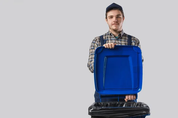 Retrato de limpiador joven en uniforme con contenedor de basura aislado en gris - foto de stock