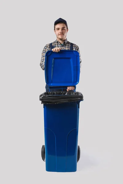Portrait of young cleaner in uniform with trash bin isolated on grey — Stock Photo