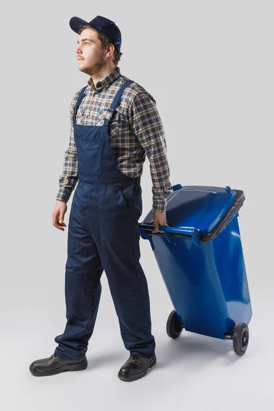 Young cleaner in uniform with trash bin isolated on grey — Stock Photo