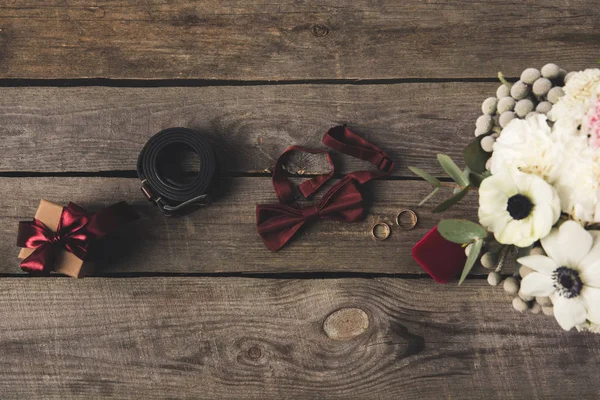 Posa piatta con fedi nuziali, portagioie, bouquet da sposa, accessori regalo e sposi su tavolo in legno — Foto stock