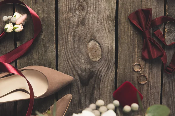 Плоская постель с туфлями для невесты, галстуком-бантом, обручальными кольцами на деревянной поверхности — стоковое фото