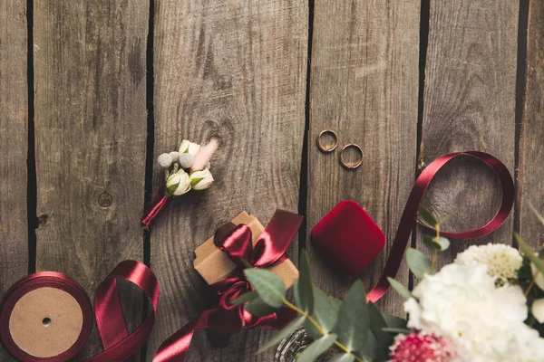 Flat lay with wedding rings, jewelry box, bridal bouquet and corsage on wooden tabletop — Stock Photo