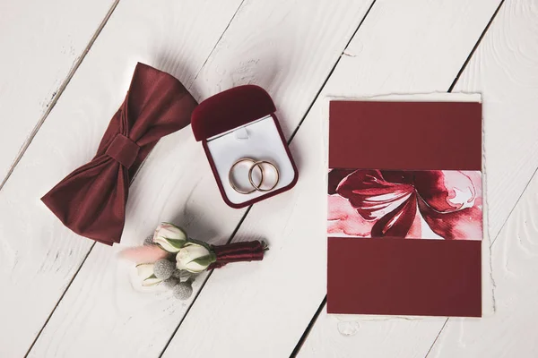 Pose plate avec invitation, boutonnière, noeud papillon et boîte à bijoux sur surface en bois — Photo de stock