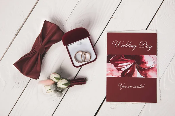 Flat lay with invitation, buttonhole, bow tie and jewelry box on wooden tabletop — Stock Photo