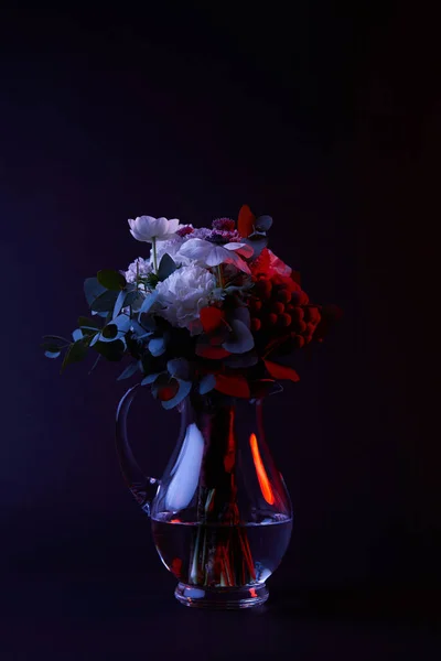 Bouquet of different flowers in reflecting glass vase on dark — Stock Photo