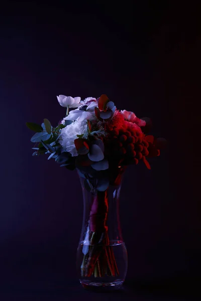 Bouquet de fleurs différentes dans un vase en verre avec lumière rouge sur sombre — Photo de stock