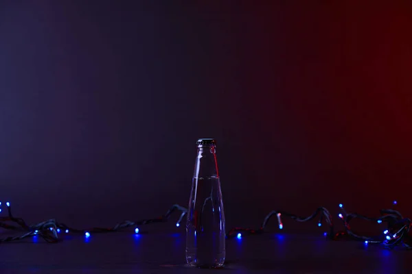 Bottle of water and blue shining garland on dark surface — Stock Photo