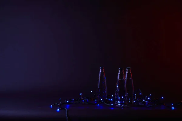 Three bottles of water with blue shining garland on dark surface — Stock Photo