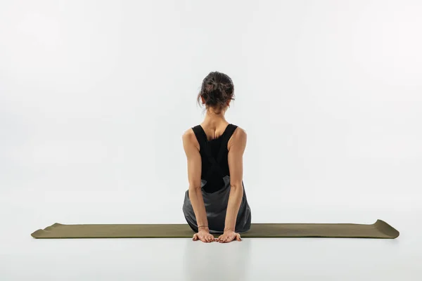 Rear view of woman practicing yoga on yoga mat isolated on white — Stock Photo