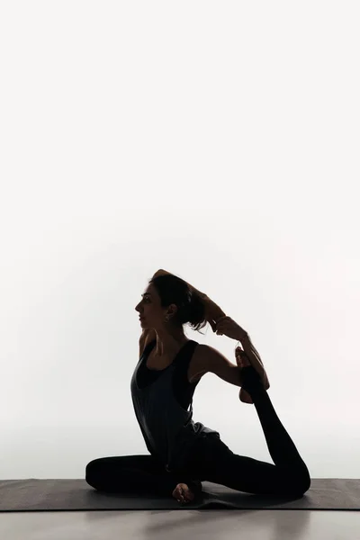 Vista laterale della donna che pratica yoga e facendo re piccione sul bianco — Foto stock