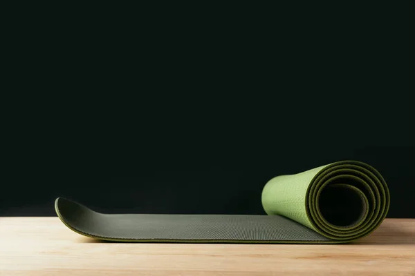 Green rolled yoga mat on wooden table on black — Stock Photo
