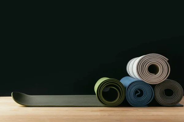 Tapetes de ioga laminados coloridos diferentes na mesa de madeira — Fotografia de Stock