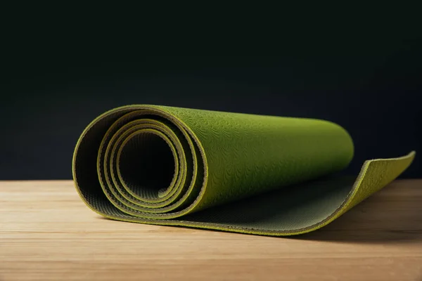 Green rolled yoga mat on wooden surface on black — Stock Photo