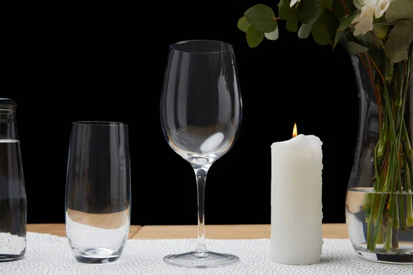 Tender flowers in vase with water bottle and empty glasses on table next to candle on black background — Stock Photo