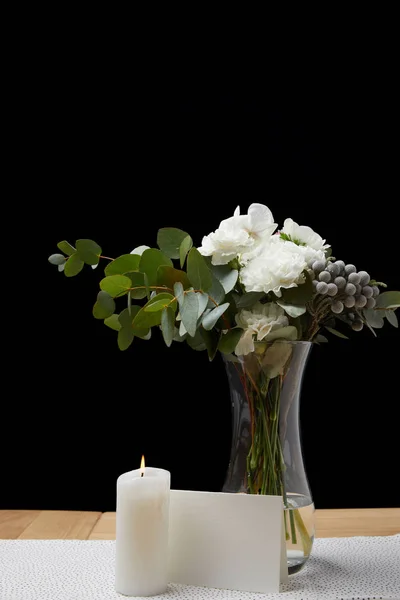Ніжні квіти у вазі з палаючою свічкою на столі поруч з порожньою карткою на чорному тлі — стокове фото