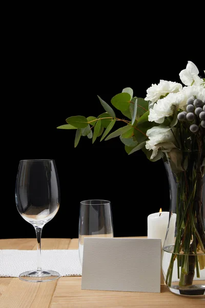 Zarte Blumen in der Vase mit Gläsern auf dem Tisch neben leeren Karten auf schwarzem Hintergrund — Stockfoto
