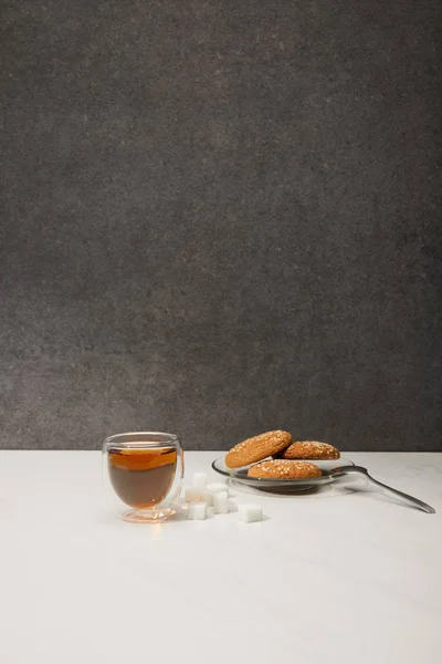 Taza de vidrio con té caliente fresco y sabrosas galletas de avena en gris - foto de stock