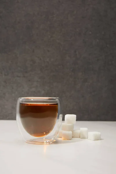 Крупный план стеклянной чашки со свежим органическим травяным чаем и кубиками сахара на сером — стоковое фото