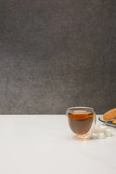 Горячий чай в стеклянной чашке, кубики сахара и вкусное печенье на сером — стоковое фото