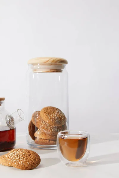 Vue rapprochée du thé dans une tasse en verre, délicieux biscuits et théière sur gris — Photo de stock