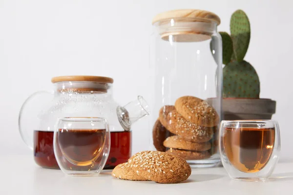 Vista de cerca del té en vasos, galletas sabrosas, tetera y cactus en olla sobre gris - foto de stock