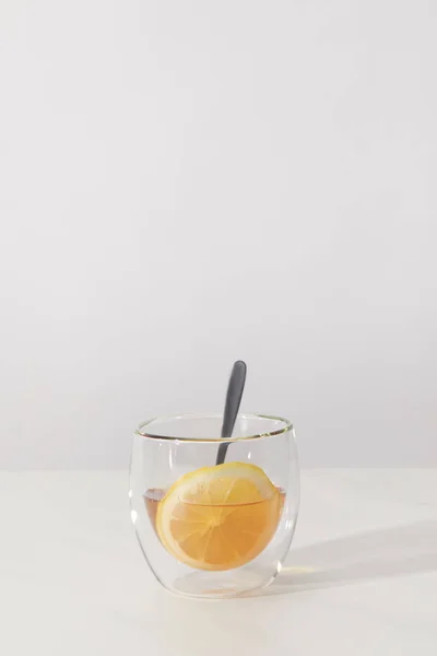 Glass cup with fresh herbal tea, spoon and slice of lemon on grey — Stock Photo