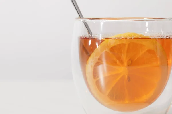 Close-up view of glass cup with fresh hot tea, spoon and slice of lemon on grey — Stock Photo