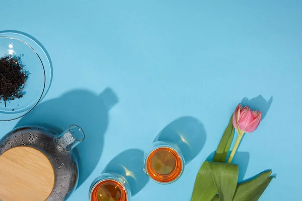 Blick von oben auf frischen heißen Tee in Tassen und Teekanne und schöne Tulpenblume auf blau — Stockfoto