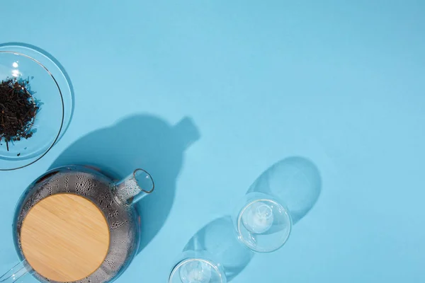 Vista superior de la tetera con té fresco, vasos vacíos y té de hierbas seco en tazón en azul - foto de stock