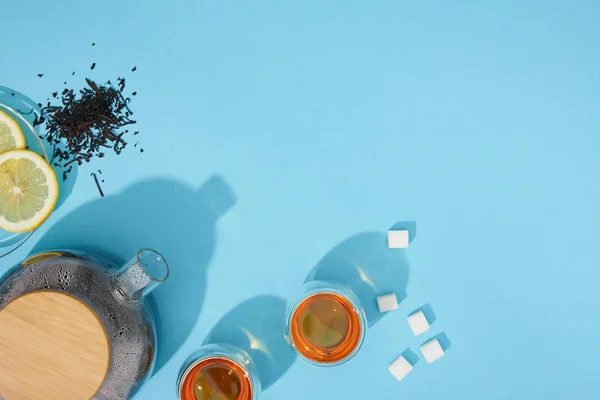 Draufsicht auf frischen Tee in Tassen und Teekannen, Zuckerwürfel, trockenen Kräutertee und Zitronenscheiben auf blauem Grund — Stockfoto