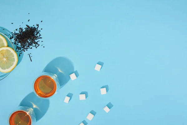 Vue du dessus de thé frais dans des tasses, des cubes de sucre, tisane sèche et citron tranché sur bleu — Photo de stock