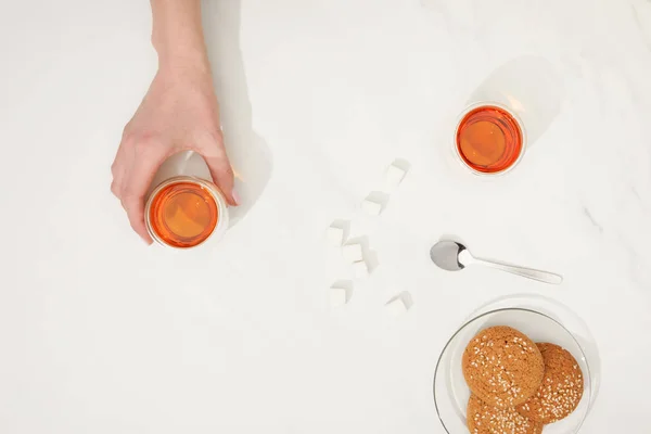 Cropped shot of human hand with cup of tea and tasty oatmeal cookies on grey — Stock Photo