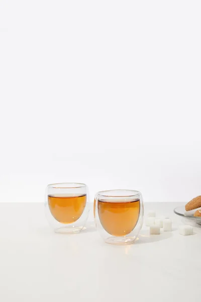 Nahaufnahme von köstlichem Tee in Glasbechern und Zuckerwürfeln mit Keksen auf grau — Stockfoto