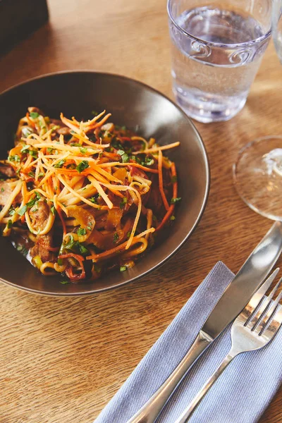 Prato com macarrão udon e porco com talheres na mesa — Fotografia de Stock