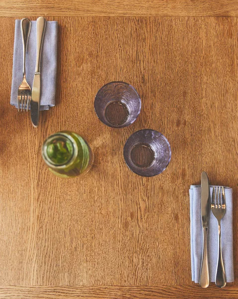 Empty glasses by bottle with mint water and cutlery on table — Stock Photo
