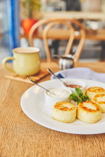 Panquecas de queijo servidas com mel e creme de leite na mesa com café — Fotografia de Stock