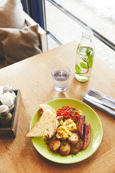 Petit déjeuner avec œufs brouillés servis dans une assiette avec légumes et saucisses — Photo de stock