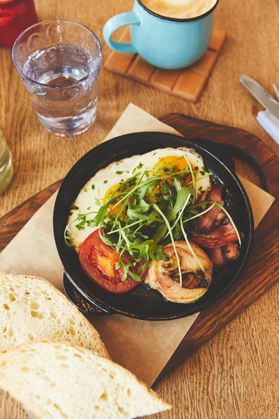 Fried eggs with tomatoes and mushrooms in pan on table — Stock Photo