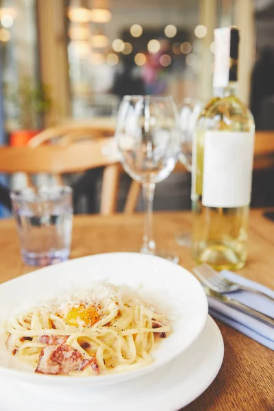 Close-up view of carbonara pasta in white plate served with white wine — Stock Photo