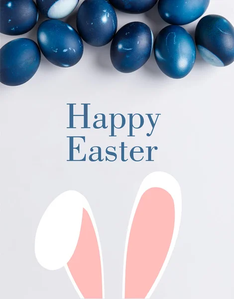 Vista superior de huevos de Pascua pintados de azul con letras de Pascua feliz y orejas de conejo en blanco - foto de stock