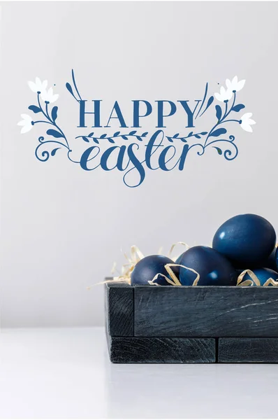 Blue painted easter eggs in box with decorative hay and happy easter lettering — Stock Photo