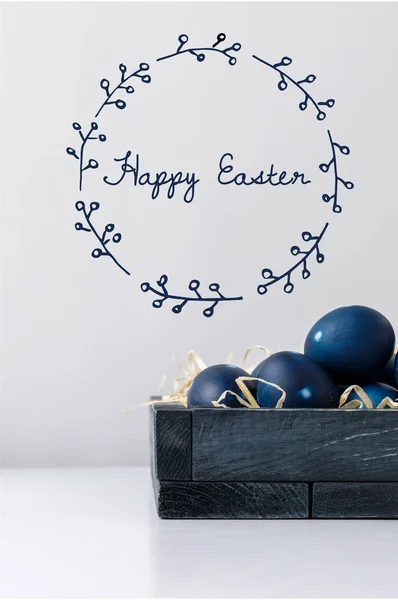 Oeufs de Pâques peints en bleu dans une boîte avec du foin décoratif et un lettrage de Pâques heureux — Photo de stock