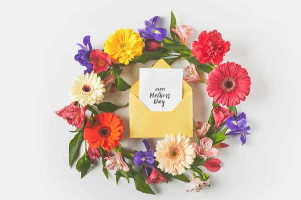 Vue de dessus de la belle couronne florale et carte de vœux de fête des mères heureux dans l'enveloppe sur gris — Photo de stock