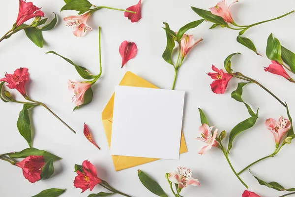 Vista superior de la tarjeta en blanco con sobre y hermosas flores de color rosa con hojas verdes en gris — Stock Photo